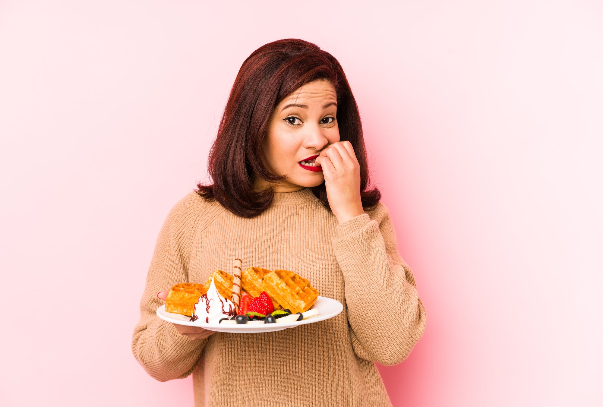 Woman with a plate full of sugary treats trying to decide if she should eat them | Parisians Pure