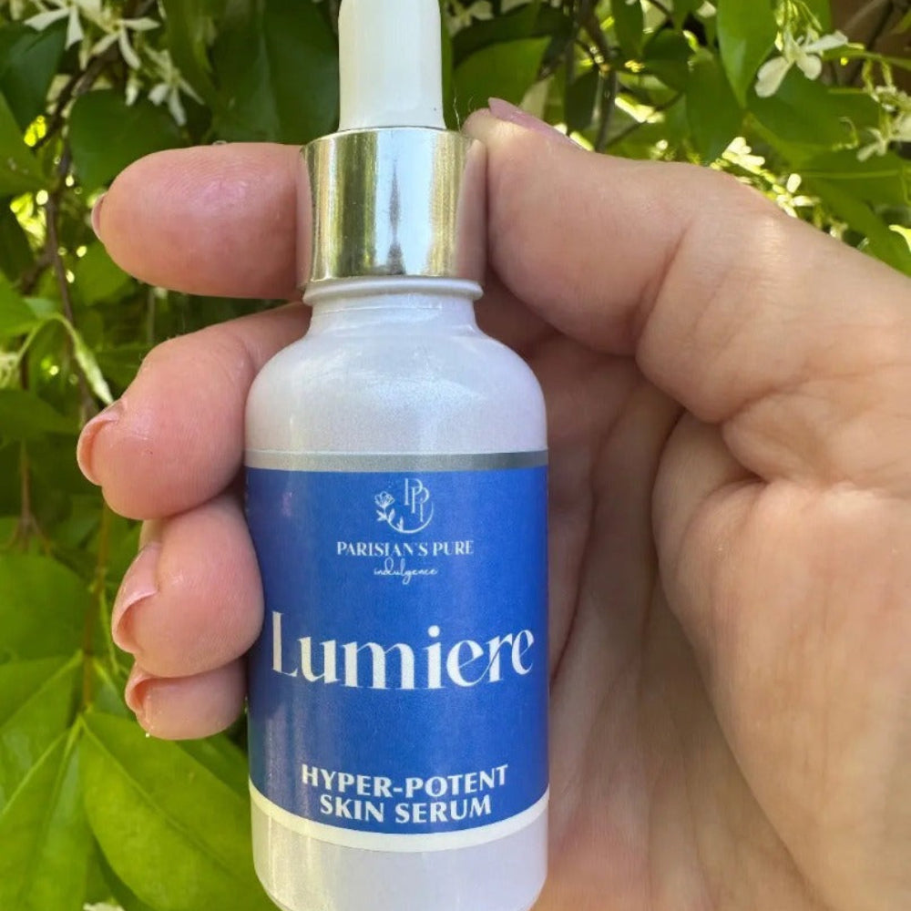 Bottle of Lumiere organic anti-aging serum with dropper for mature skin being held in hand with greenery behind