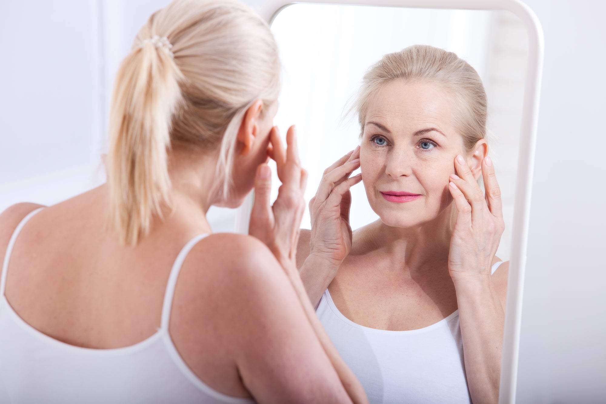 Woman over 50 looking at her skin in a mirror