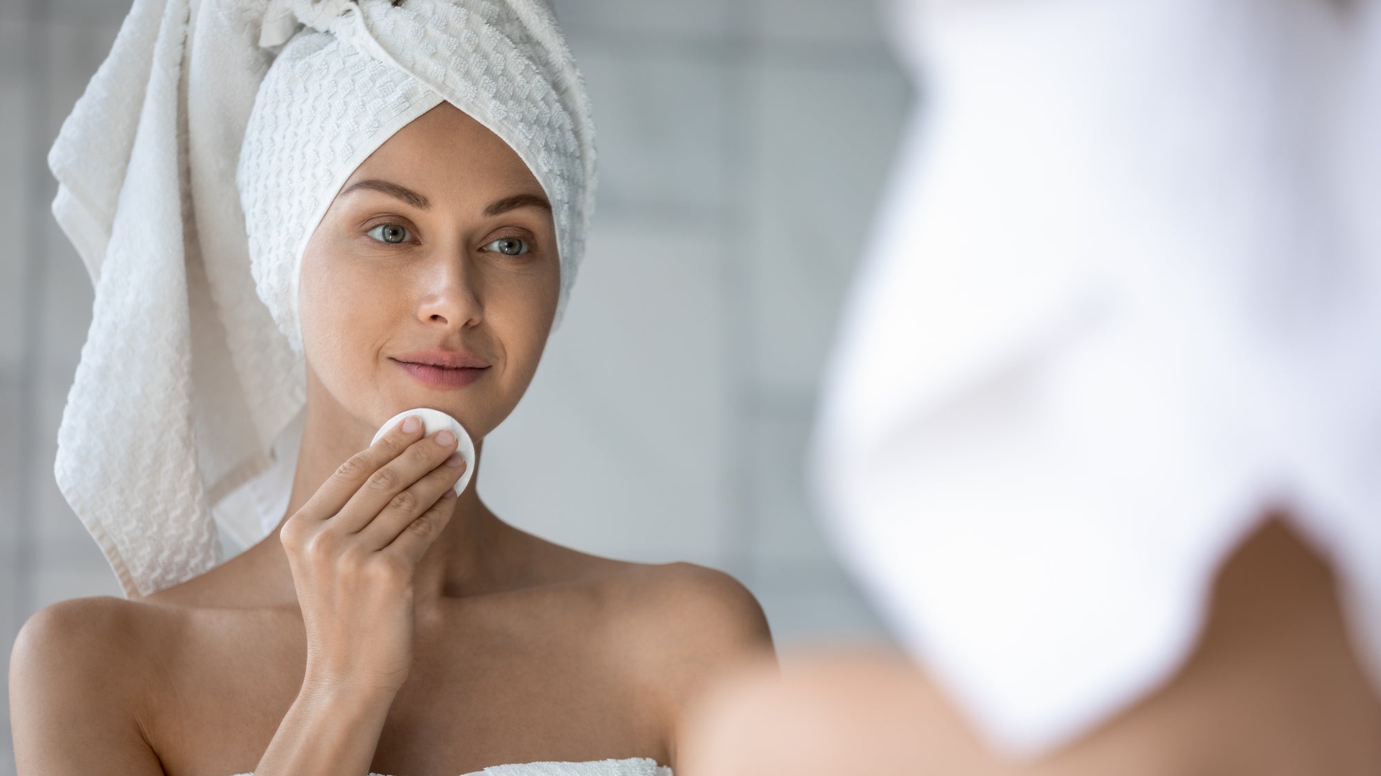 women looking in mirror and cleansing her face with cotton pad, Parisians Pure Skincare